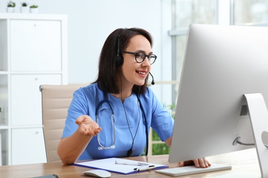Doctor with headset and computer consulting patient online in office. Hotline service