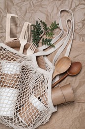 Photo of Net bag with different eco items on crumpled paper, top view. Recycling concept