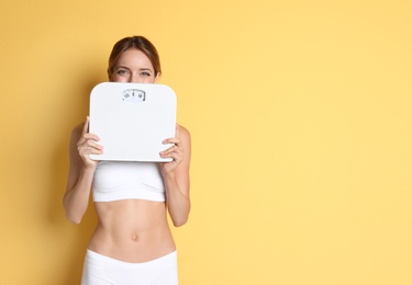 Photo of Happy slim woman satisfied with her diet results holding bathroom scales on color background
