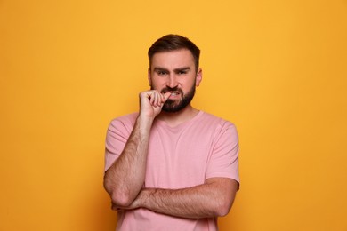 Man biting his nails on yellow background. Bad habit