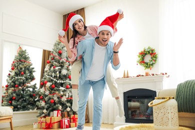 Happy couple in Santa hats near Christmas tree at home