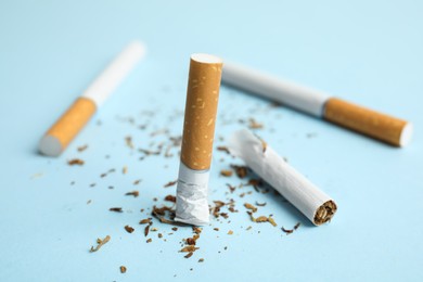 Broken and whole cigarettes on light blue background, closeup. Quitting smoking concept