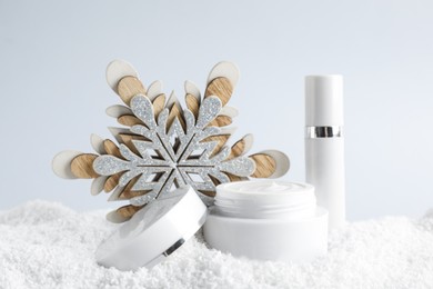 Jar of hand cream and lip balm near decorative snowflake on snow against light background. Winter skin care cosmetics