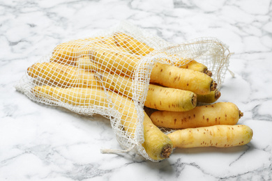 Many raw white carrots in mesh bag on marble table