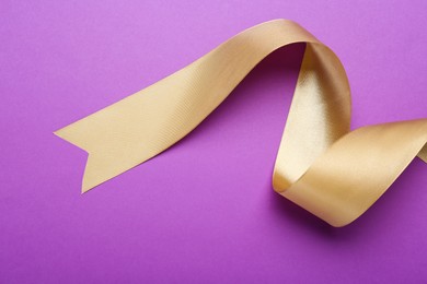 Photo of Beautiful golden ribbon on purple background, top view