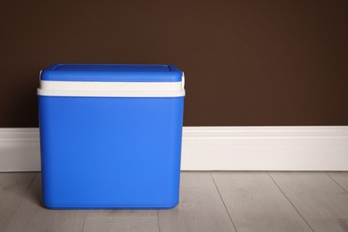 Closed blue plastic cool box near brown wall. Space for text