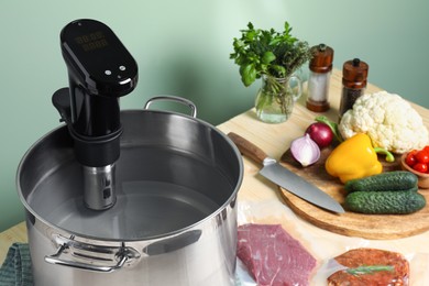 Pot with sous vide cooker, meat in vacuum packing and other ingredients on wooden table. Thermal immersion circulator