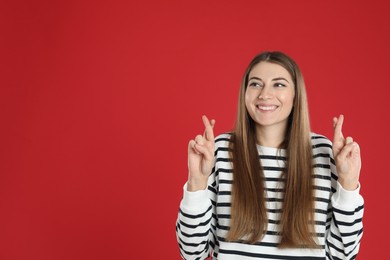 Woman with crossed fingers on red background, space for text. Superstition concept