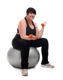 Happy overweight mature woman with dumbbells sitting on fitness ball against white background