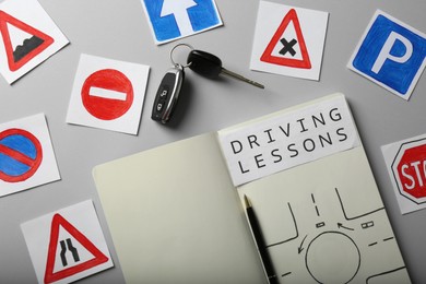 Photo of Flat lay composition with workbook for driving lessons and road signs on light grey background. Passing license exam
