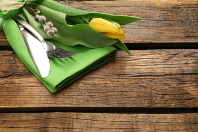 Cutlery set with beautiful willow branch and tulip on wooden table, space for text. Easter celebration