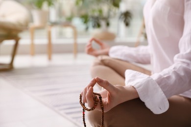 Woman with beads meditating at home, closeup. Space for text