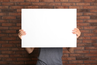 Woman holding white blank poster near red brick wall. Mockup for design