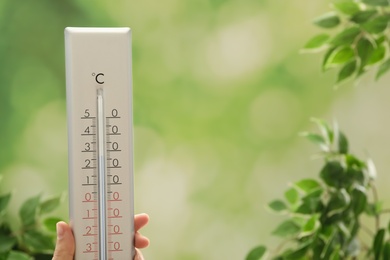 Woman with weather thermometer on blurred background, closeup. Space for text