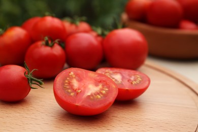 Photo of Cut and whole red tomatoes on wooden board against blurred background, closeup
