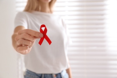 Woman holding red awareness ribbon on light background, closeup with space for text. World AIDS disease day