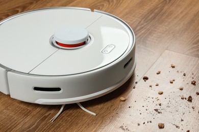 Photo of Robotic vacuum cleaner removing dirt from wooden floor indoors, closeup