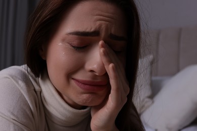 Sad young woman crying on bed at home, closeup. Loneliness concept