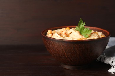 Photo of Bowl of tasty hummus with chickpeas and parsley on wooden table, space for text