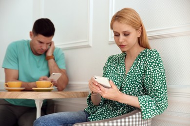 Man and young woman preferring smartphones over speaking with each other during first date in cafe