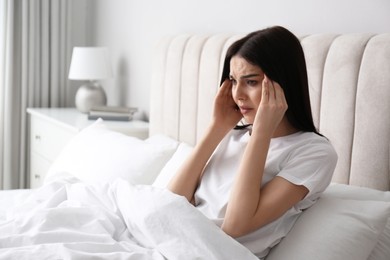 Young woman suffering from migraine in bed at home, space for text