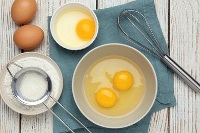 Whisk, eggs in bowl and flour on white wooden table, flat lay