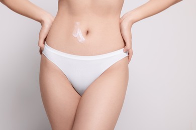 Photo of Woman with body cream smear on belly against light grey background, closeup. Space for text