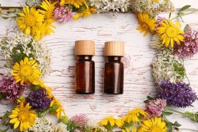 Flat lay composition with bottles of essential oils surrounded by beautiful flowers on white wooden table