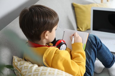 Cute little boy with headphones and modern laptop studying online at home. E-learning