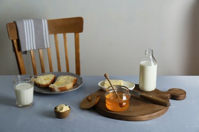 Photo of Jar with honey, milk, butter and bread served for breakfast on grey table indoors