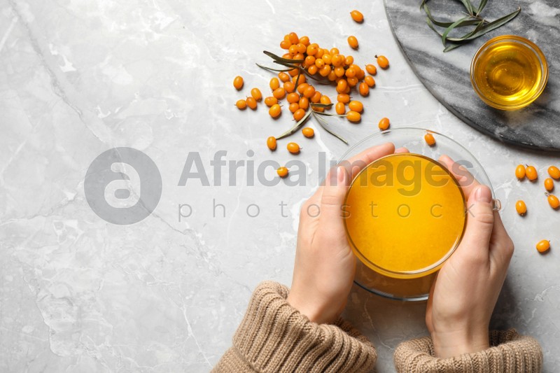 Woman holding cup with sea buckthorn tea at grey table, top view. Space for text