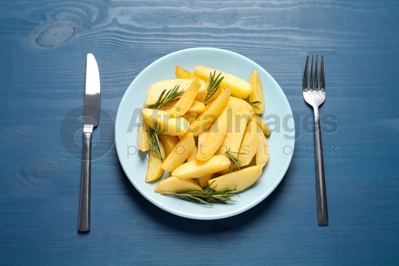 Photo of Plate with tasty baked potato wedges and rosemary on blue wooden table, flat lay