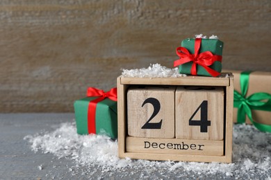 December 24 - Christmas Eve. Wooden block calendar and gift boxes on grey table, space for text
