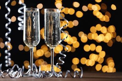 Glasses of champagne and serpentine streamers against black background with blurred lights. Space for text