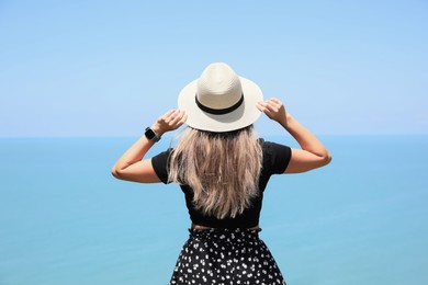 Woman with hat near sea on sunny day, back view