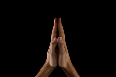 Man praying against black background, closeup view