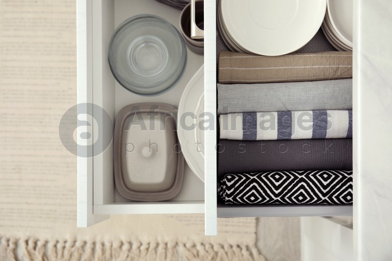 Photo of Open drawers of kitchen cabinet with different dishware and towels, top view