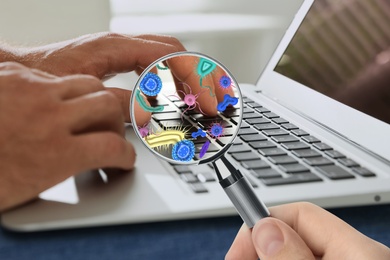 Image of Man with magnifying glass detecting microbes on laptop keyboard, closeup