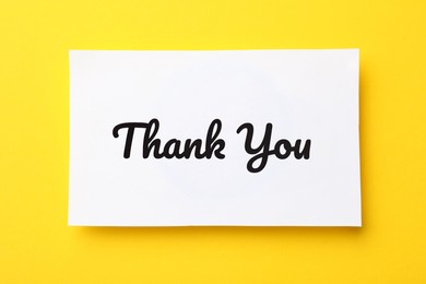 White paper note with phrase Thank You on yellow background, top view