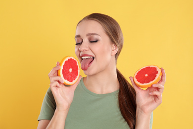 Young woman with cut grapefruit on yellow background. Vitamin rich food
