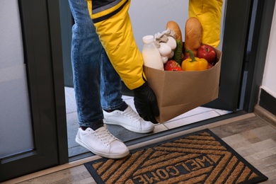 Courier bring paper bag with food to doorway, closeup. Delivery service during quarantine due Covid-19 outbreak