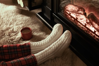 Woman in knitted socks resting near fireplace at home, closeup of legs