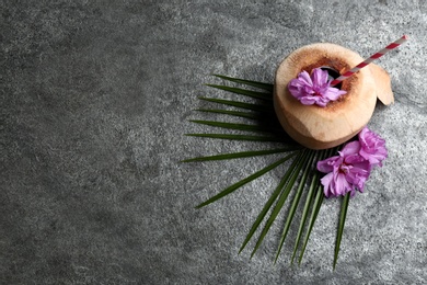 Young peeled coconut with straw, palm leaf and flowers on grey table, flat lay. Space for text