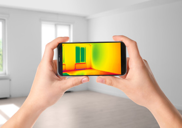 Woman detecting heat loss in room using thermal viewer on smartphone. Energy efficiency
