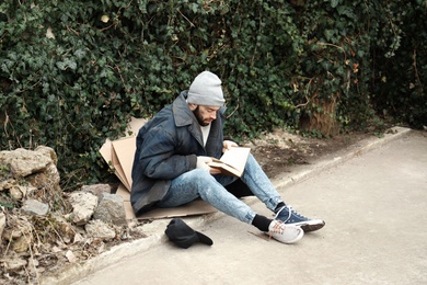 Poor homeless man with book on street in city