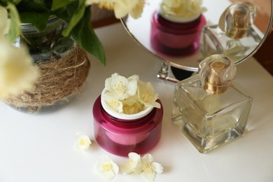 Jar of cream with beautiful jasmine flowers, perfume and mirror on white table