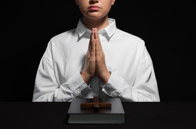 Woman holding hands clasped while praying at table with Bible and cross, closeup