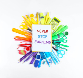 Notebook with phrase NEVER STOP LEARNING and different school stationery on white background, top view