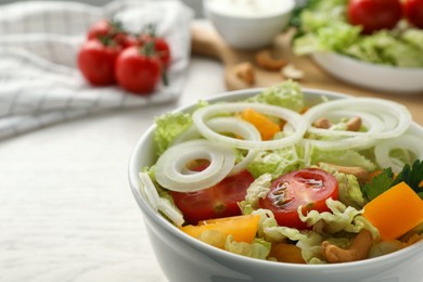 Bowl of delicious salad with Chinese cabbage, tomatoes and onion on white wooden table, closeup