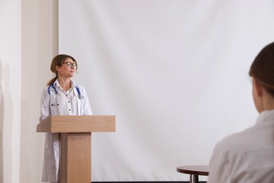 Photo of Doctor giving lecture near projection screen in conference room, space for text